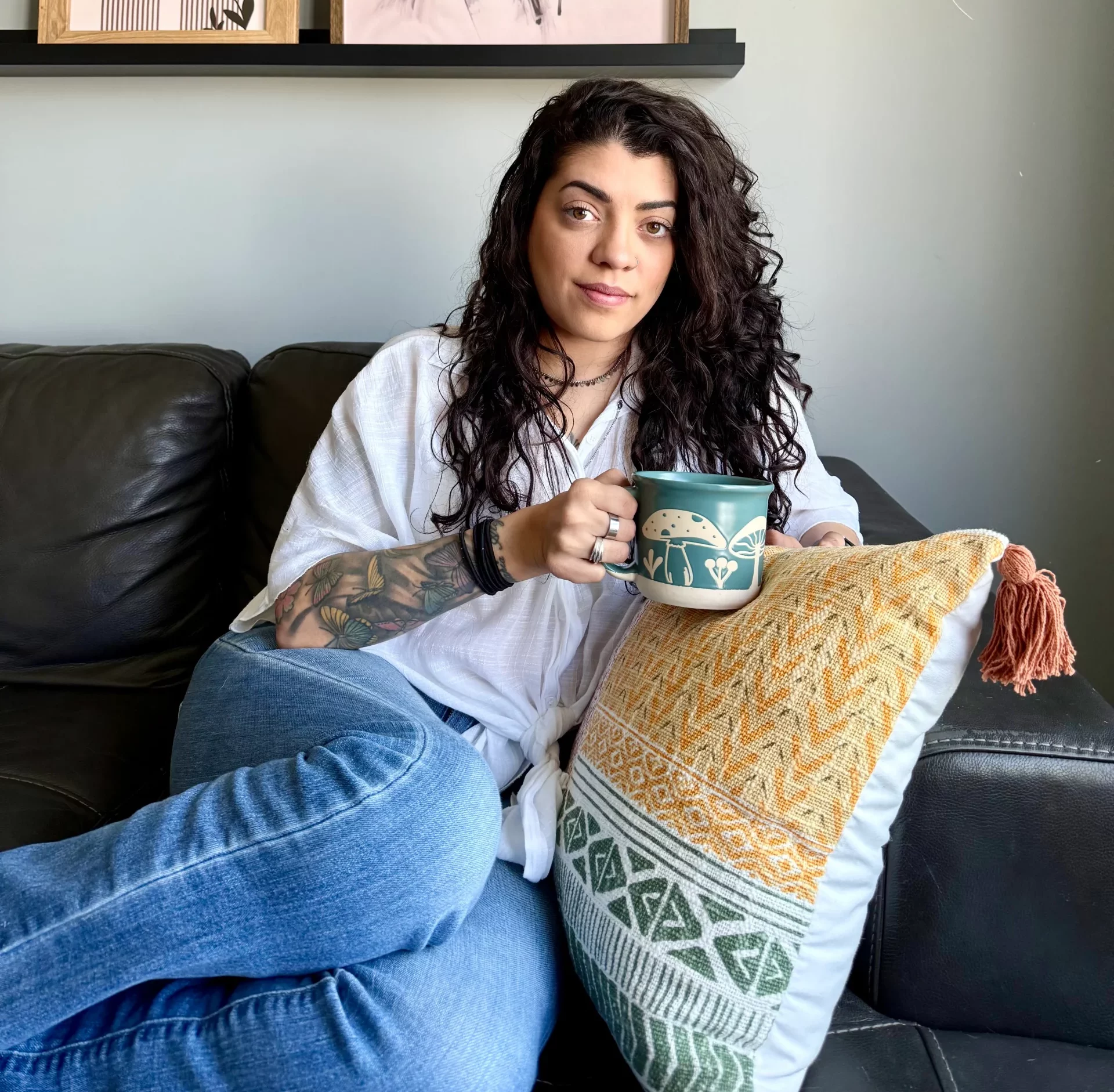 Kira sentada en un sofá, sonriendo y disfrutando de una taza de café, en un momento relajado y cercano.